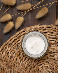 Fototapeta na wymiar Opened cream jar on wattled placemat near Hare's Tail grass top view. Cosmetic Mockup