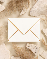 Envelope near beige travertine stones and dried pampas grass top view, greeting mockup