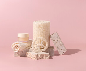 Face towel, loofah sponges and cream jar on stones on light beige close up. Mockup