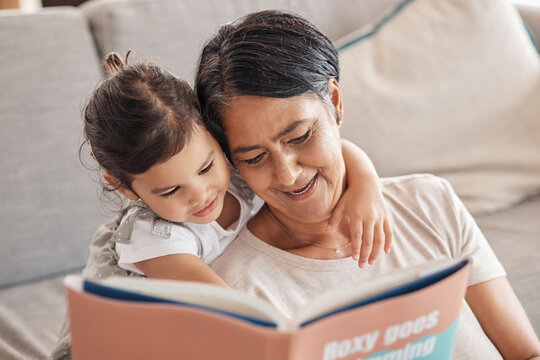 Education, Learning And Girl And Grandmother Reading A Book On A Sofa, Relax And Bonding In Living Room. Children, Love And Storytelling By Senior Woman Enjoying Fantasy Story With Curious Grandchild