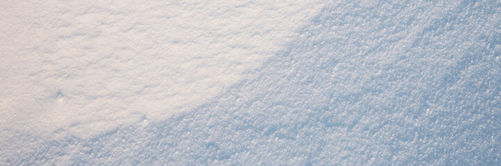 Beautiful winter background with snowy ground. Natural snow texture. Wind sculpted patterns on snow surface. Wide panoramic texture for background and design. Closeup top view with copy space.