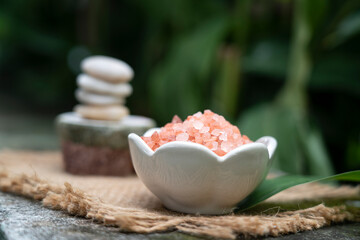 pink himalaya salt in white ceramic bowl in front of  meditation stack stone  on green blurred background,  aromatherapy spa set concept.