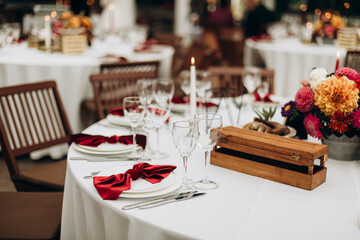 decorated served table with a decorative bouquet of flowers in the middle. a round table with a white tablecloth and white dishes with a red napkin tied in a bow, transparent glasses and silver cutler