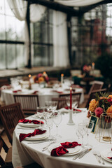decorated served table with a decorative bouquet of flowers in the middle. a round table with a white tablecloth and white dishes with a red napkin tied in a bow, transparent glasses and silver cutler