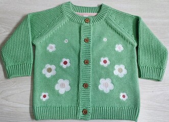 Girls knitted front buttoned and flowers embroidery pattern crew neck green colour sweater and cardigan isolated on wooden background. Children's and kids clothes. Front closeup view.