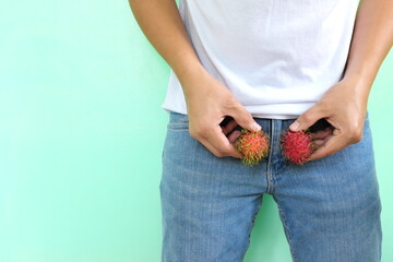 Male testicle health and nutrition, itchy, red, hairy and swollen balls concept. Young asian man holding two red fruits on crotch area.