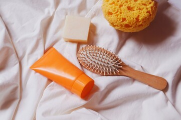 Orange tube moisturizing cream, natural soap, wooden hair brush and yellow sponge. Travel beauty products, cosmetic essentials flat lay photography