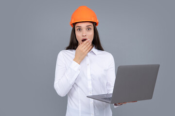 Surprised shocked excited business woman with laptop computer, portrait on gray. Young woman in helmet hold laptop computer on gray background. Architect businesswoman.