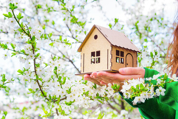 Toy house model in hands under a blooming tree