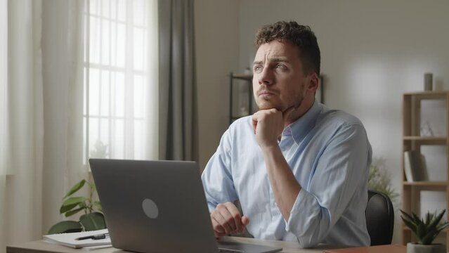 Young male employee sit at workplace desk with laptop and thinks over creative task