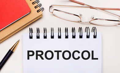 On a light background - glasses in gold frames, a pen, brown and red notepads and a white notebook with the text PROTOCOL. Business concept