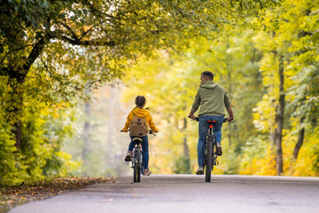Happy father and daughter ride bicycles in autumn park on sunny day.