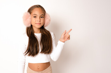 Full length portrait of brunette hispanic girl in earmuffs showing and pointing up with fingers...