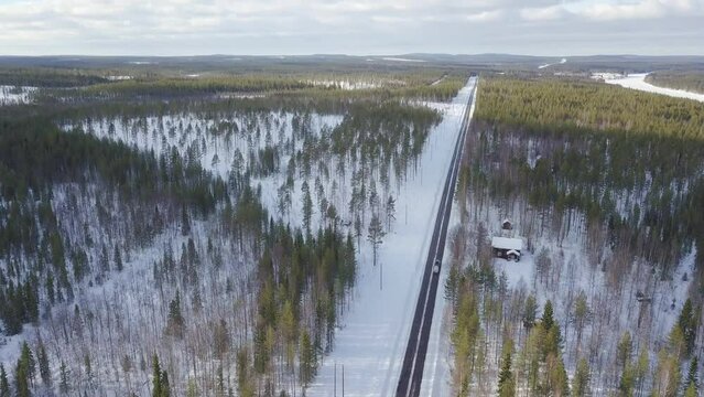Cinematic drone aerial backward and tilt up move. Cars driving onthe ice covered road middle of endless forest in finnish Lapland. Small  lappish cottage by the road side.