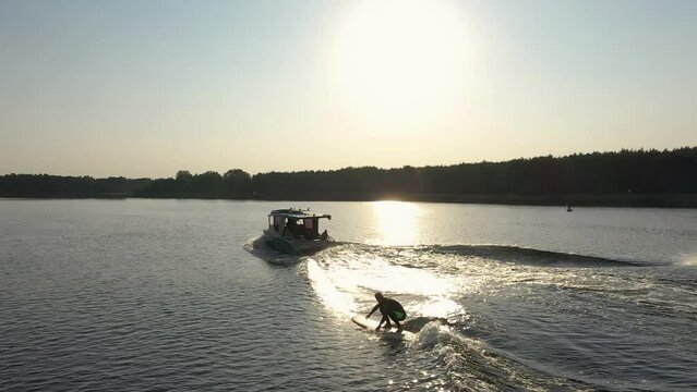 surfer on surfboard surfing waves behind boat in sunset 001