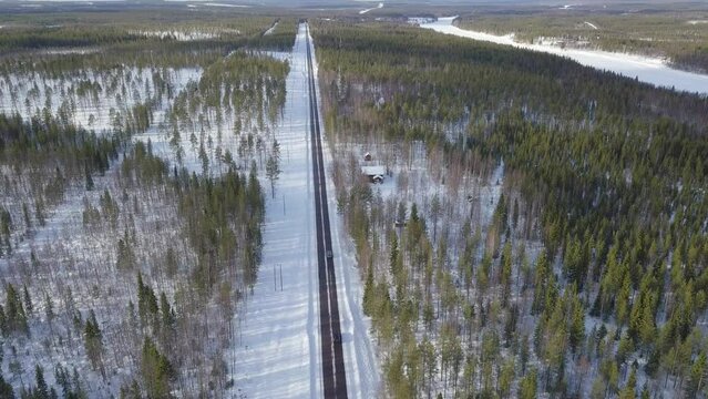 Steady shot above the road. Two cars coming from down side of image and driving away. Black line road middle of endless forest of Lapland in Finland. Small abandoned cottage site by the road.