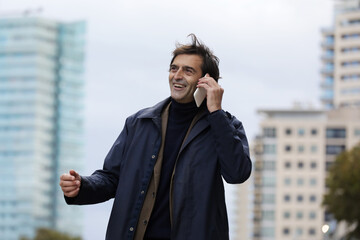 Smiling senior man, businessman talking on the phone while walking around the city,