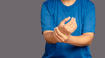 Close-up of hands young man suffering from wrist pain while standing on a gray background