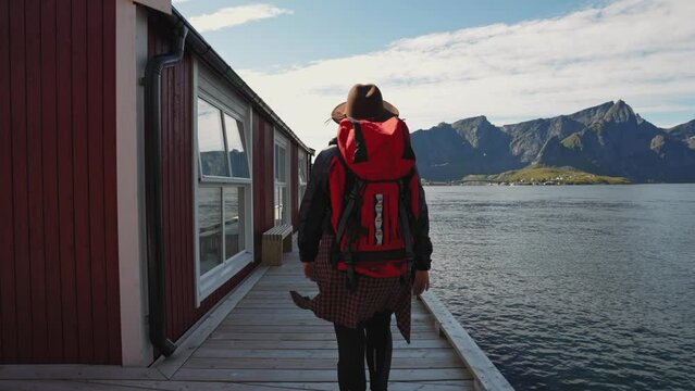 Beautiful young girl traveler go to the wooden pier on the background of traditional red rorbu traveling to Lofoten Norway