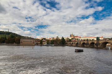Look over Vltava river to Charles bridge, Prague Castle in background under blus sky with white clouds.