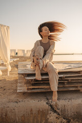 Image of beautiful young caucasian girl sitting on wooden pallet with her eyes closed. Model is waving brown straight hair, wearing brown outfit. Body and soul concept