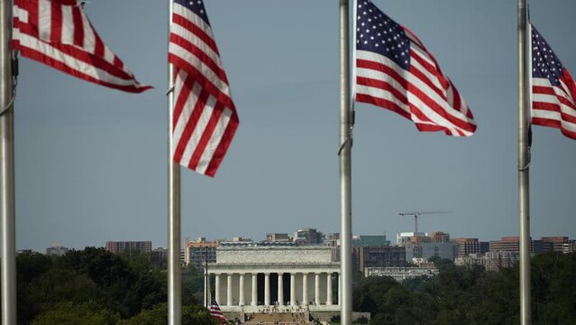 Distant closeup view of Lincoln Memorial Arlington, VA, and airplane landing through the flags waving in the wind at the Washington Monument in Washington DC.
