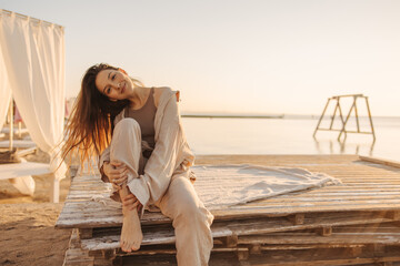 Lovely young caucasian woman in good mood is spending time enthusiastically on seashore alone. Her brown, straight hair blows in wind. Relaxation and peace concept.