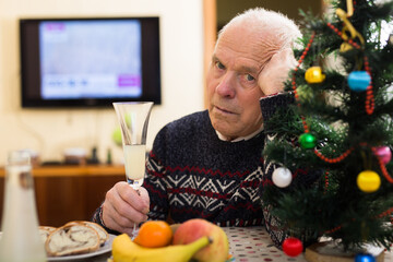 Upset ederly man sitting alone at home table at Christmas