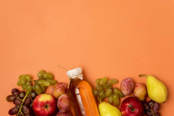 Bottle With Apple Cider or Vinegar with Raw Autumn Fruits on Orange Background Top View Copy Space