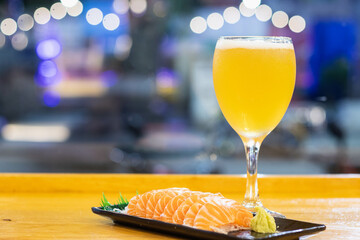 Craft beer in wine glass and salmon sashimi placed on a wooden table with lamp bokeh in the...