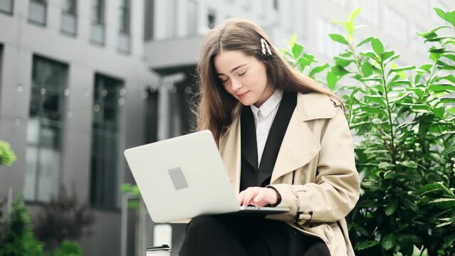Young business woman in classic suit using laptop while sitting near business centre. Attractive woman texting on laptop and works distantly.