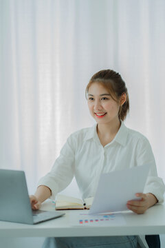 Beautiful Asian woman smiling happily relaxing using laptop computer in office. creative young girl working and typing on keyboard online work concept vertical picture