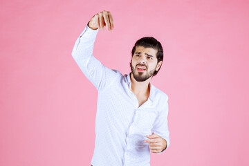 Person in white shirt holding a glass in front of a pink background, celebrating or making a toast with a cheerful gesture