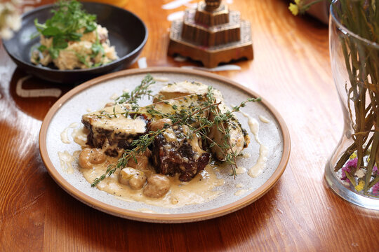 Beef cheek in creamy boletus sauce with thyme, served with campfire potatoes and truffle oil, on a plate, on wood table