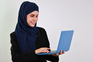 Happy smart asian business woman in muslim dress standing while using computer and smiling with confident in studio. Isolated white background portrait with beautiful face in hijab.