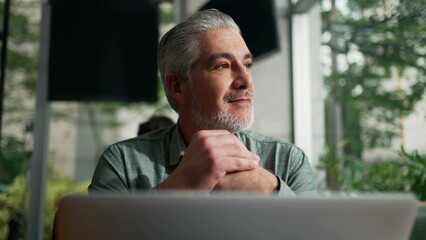 Thoughtful older businessman seated at coffee shop in contemplation. Pensive senior executive thinking about business looking out window