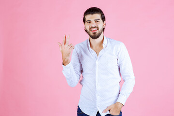 Young man in white shirt making a peace sign gesture against a pink background