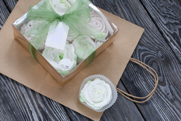 Homemade marshmallows in a gift box. Tied with ribbon. Paper bag from craft paper. Zephyr flowers. On black pine boards. Taken from above.