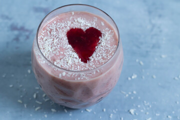 Berry smoothie with a heart of jam in a glass. Coconut chips Grey background. Top view.