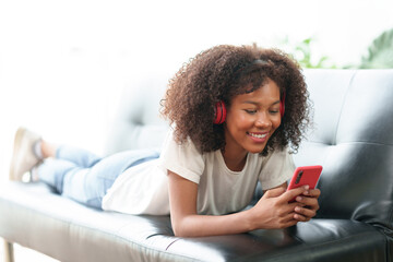 Bright and cute Asian young woman wearing headphones sit on the sofa and using smartphone to listen to music happy and relax listening to music at home.