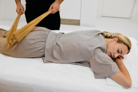 Woman getting anti-stress massage with bamboo sticks at massage salon. Bamboo brooms in masseur hands in motion