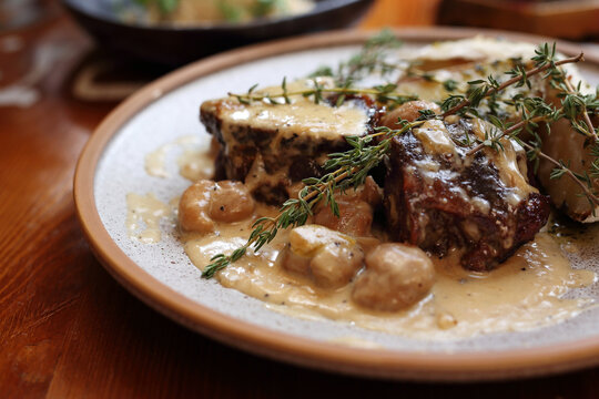 Beef cheek in creamy boletus sauce with thyme, served with campfire potatoes, on a plate, on wood table, close-up.