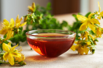 A bowl of red St. John's wort oil with fresh Hypericum flowers