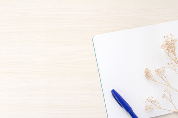 open notebook, blue pen and dried flowers on beige wood desk