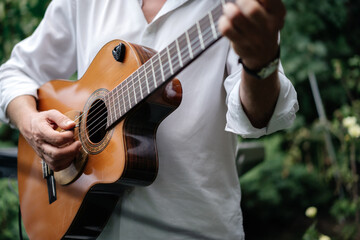 Classical guitar in the hands of a man musician in a white suit. Music in the open space in the...