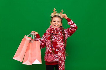 A little girl in a Christmas sweater holds bags with gifts from the store and smiles. A child doing Christmas shopping on an isolated background.