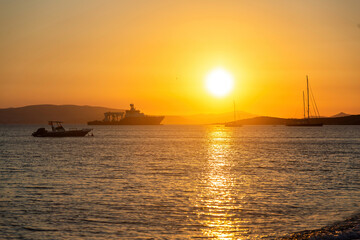 Fototapeta na wymiar Naxos island, sunset over Aegean sea, Cyclades Greece. Sundown beams colors ships, water, sky.
