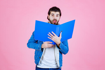 Man opening a blue folder and hiding his face behind it