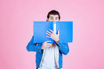 Man opening a blue folder and hiding his face behind it
