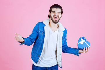 Man holding a blue heart shaped gift box and looking happy